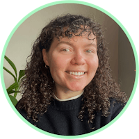 a woman with curly hair smiling in front of a plant